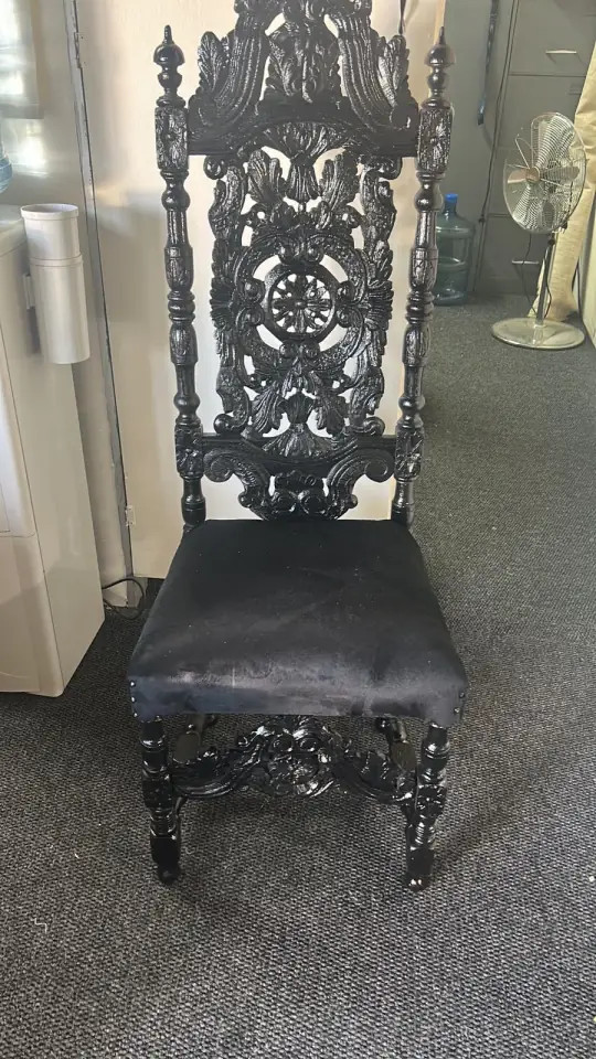 A tall carved chair with a black velvet seat
