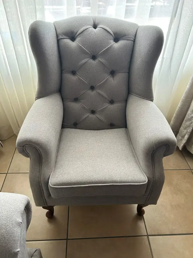 A wingback chair in grey, with a buttoned back